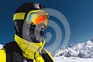 Close-up portrait of a skier in a mask and helmet with a closed face against a background of snow-capped mountains and