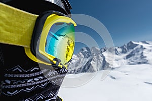 Close-up portrait of a skier in a mask and helmet with a closed face against a background of snow-capped mountains and