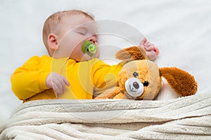 Close-up portrait of a sleeping baby in an embrace with a toy and a pacifier in his mouth