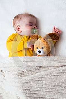 Close-up portrait of a sleeping baby in an embrace with a toy and a pacifier in his mouth. Vertical photo