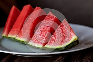 A close up portrait of a sliced up quarter of a watermelon. The fruit is red in the middle with black seeds and has a green