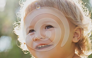 Close up portrait of a small blond baby boy. Funny kids cropped face outdoor on sunny day. Kids smiling, cute smile.