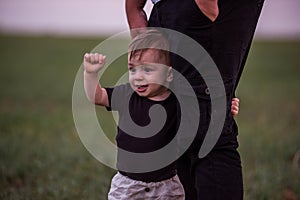 Close-up portrait of small boy looking curiously ahead while being held securely by parents hand