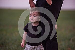 Close-up portrait of small boy looking curiously ahead while being held securely by parents hand
