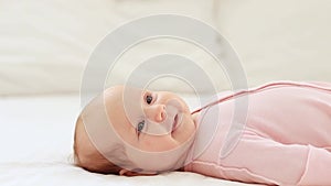 close-up portrait of a small newborn baby girl with blue eyes lies on a white cotton bed at home and smiles