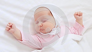 close-up portrait of a small newborn baby girl sleeping on a white cotton bed at home and stretching in her sleep