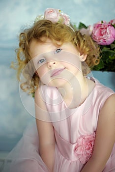 Close up portrait of small 5 years old blonde curly girl in beautiful princess dress with pink flowers on background. Little girl