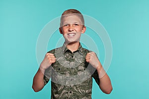 Close-up portrait of a blonde teenage boy in a green shirt with palm print posing against a blue studio background