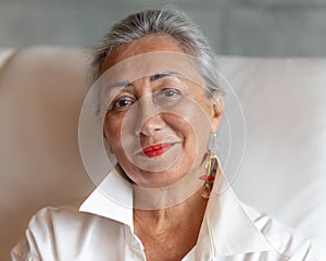 Close-up portrait of a smiling adult woman in a white shirt on a white sofa