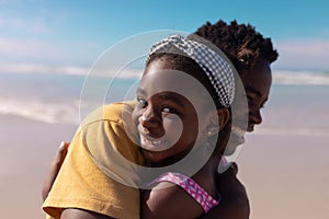 Close-up portrait of smiling african american girl embracing young father against sea and sky