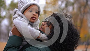 Close-up portrait of smiling African American young woman spinning cute baby boy enjoying leisure in autumn park with