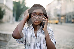 Close up portrait of a smiling african woman in glasses, walking in the old city with cellphone, talking with her friend