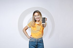 Close up portrait of a smiling asian woman showing blank screen mobile phone while standing isolated over gray