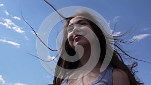 Close up portrait of smiling beautiful young girl on the blue sky background with blowing hair in wind