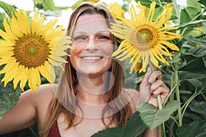 Close up portrait of smiling blond woman holding yellow flowers in sunflower field