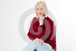 Close up portrait of smiling blond woman in stylish red shirt sitting on chair on white background