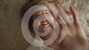 Close-up portrait of smiling caucasian blond woman lying on soft bed in sun rays. Happy young girl resting indoors