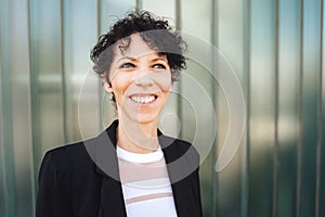 Close up portrait of smiling Caucasian businesswoman looking away while standing against green wall