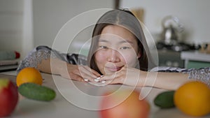 Close-up portrait of smiling charming Asian woman posing in kitchen indoors. Happy beautiful lady with brown eyes