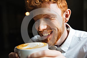 Close-up portrait of smiling curly readhead bearded man tasting