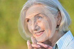 Close-up portrait of smiling elderly woman posing in summer park