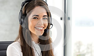 Close up portrait of smiling female customer service consultant with headset talking with client during phone call.