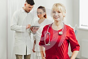 Close-up portrait of a smiling female doctor in a red uniform with a stethoscope.