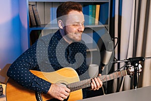 Close-up portrait of smiling guitarist singer man playing on acoustic guitar and singing into microphone recording song