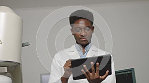 Close up portrait of smiling handsome African Doctor holding digital tablet pc. Doctor, standing in front of ultrasound