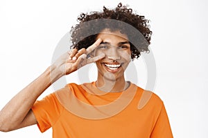 Close up portrait of smiling hispanic man showing peace, v-sign near eyes and looking happy, positive people and