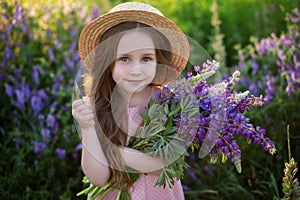 Close up portrait of a smiling little girl in a straw hat and with a large bouquet of lupins. A child girl in a field of lupines.