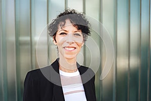 Close up portrait of smiling mature business woman in suit standing against green wall