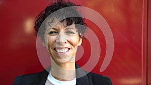 Close up portrait of smiling mature business woman in suit standing against red wall