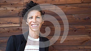 Close up portrait of smiling mature business woman in suit standing against wooden wall