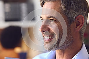 Close Up Portrait Of Smiling Mature Businessman At Desk In Modern Office