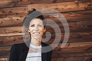 Close up portrait of smiling mature businesswoman in suit standing against wooden wall