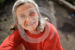 Close up portrait of a smiling senior woman with grey hair and face with wrinkles outdoors relaxing at park during sunny