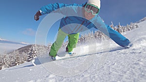 CLOSE UP, PORTRAIT: Smiling snowboarder doing hand drag in fresh powder snow photo