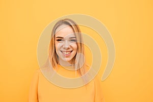 Close-up portrait of a smiling teenage girl on a orange background, wearing a casual clothing, looking into the camera and