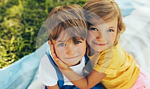 Close up portrait of smiling two children playing on the blanket outdoors. Sister hugging her little brother in the park. Kids