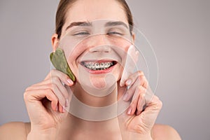 Close-up portrait of a smiling woman with braces on her teeth holding two gouache scrapers near her face.