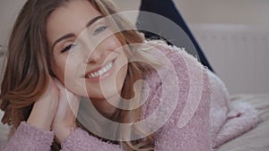 Close up portrait of smiling woman lying on bed and looking at camera.