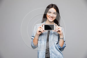 Close up portrait of a smiling woman showing blank screen mobile phone while standing isolated over gray background