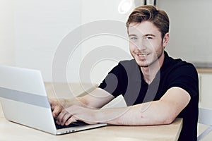 Close up portrait of a smiling young caucasian man working at home on laptop sitting at desk.