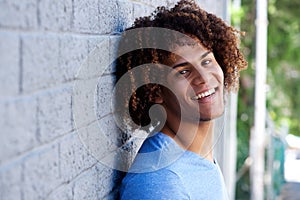 Close up portrait of smiling young man leaning against wall