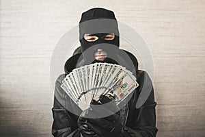 Close up portrait of sneaky burglar with black mask, gloves counting money on white background. focus on money.
