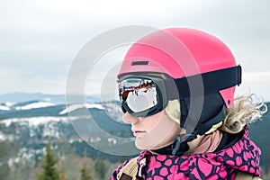 Close up portrait of snowboarder woman at ski resort wearing helmet and goggles with reflection of mountains.