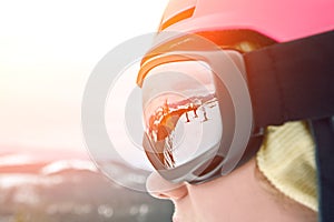 Close up portrait of snowboarder woman at ski resort wearing helmet and goggles with reflection of mountains. Sun flare