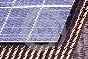 A close up portrait of solar panels lying on an orange tile roof. The photovoltaic cells of the green ecological energy producing