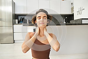 Close up portrait of sportswoman, fitness woman massaging her neck, warm-up her body after workout, doing yoga on rubber